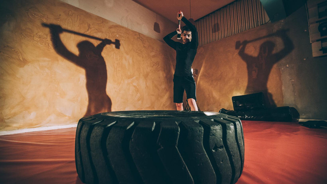Male athlete inside a gym hitting a tyre with a large rubber hammer